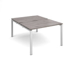 Large modular bench desk with a grey wood-effect top, integrated cable access cut-out, and silver metal legs, shown on a white background.