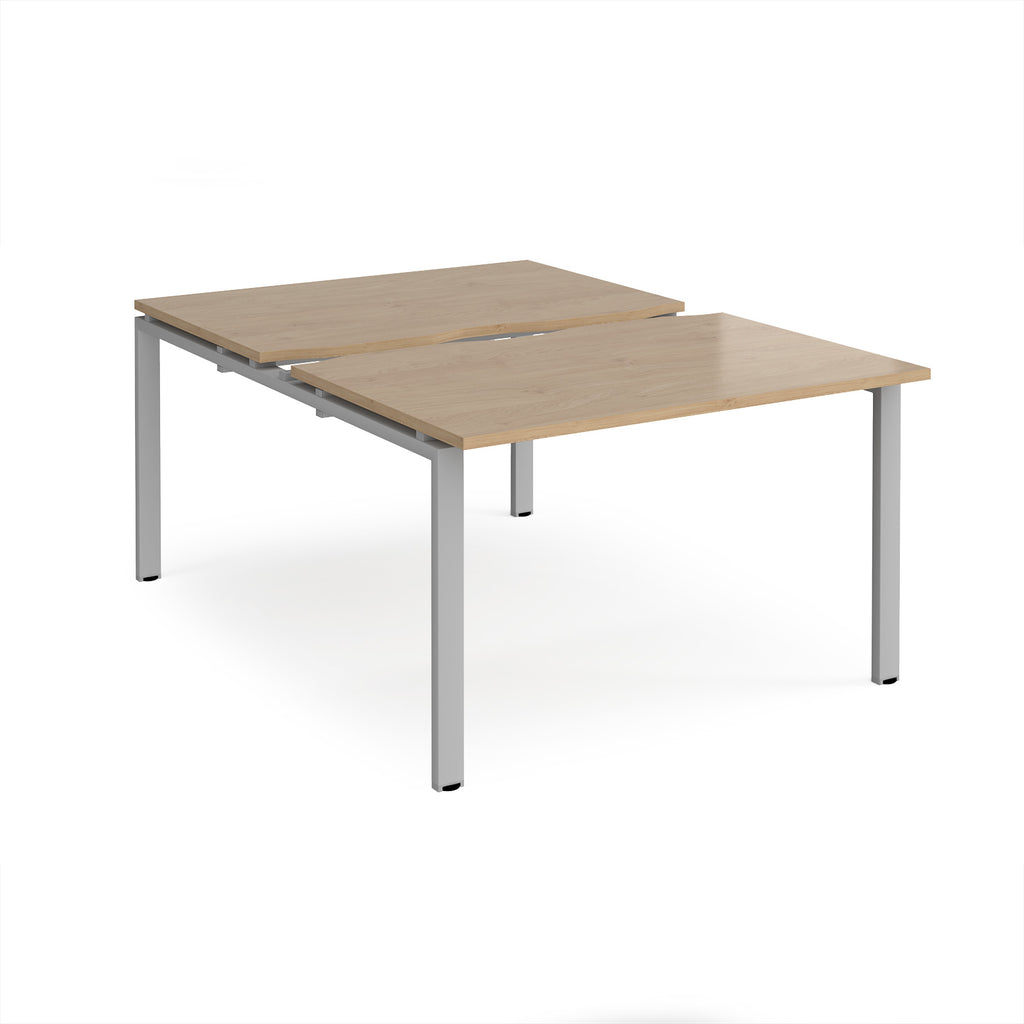 Large modular bench desk with a wood-effect top, integrated cable access cut-out, and silver metal legs, shown on a white background.