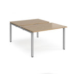 Large modular bench desk with a wood-effect top, integrated cable access cut-out, and silver metal legs, shown on a white background.