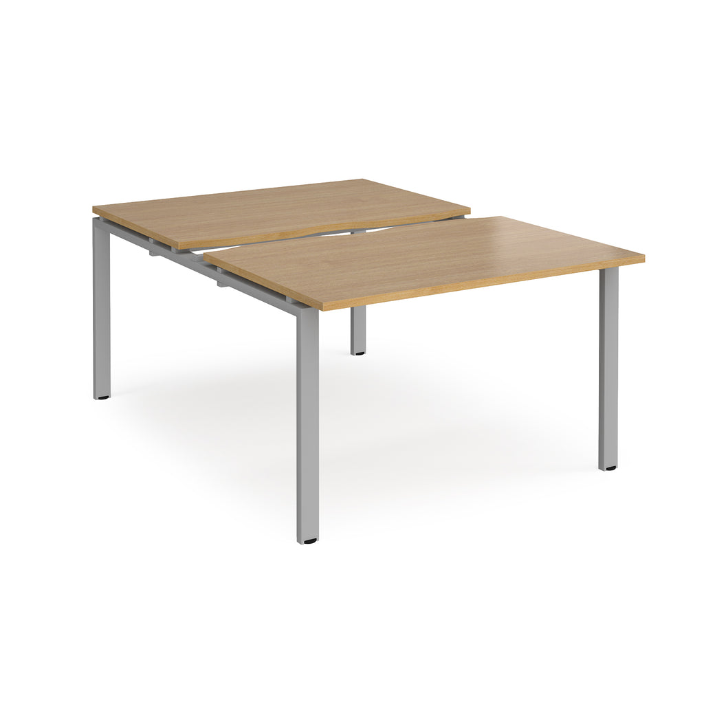 Large modular bench desk with a wood-effect top, integrated cable access cut-out, and silver metal legs, shown on a white background.