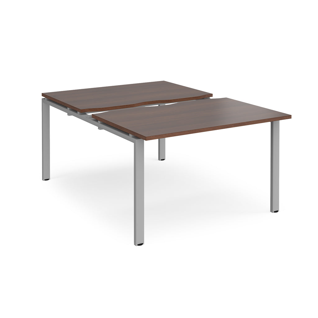 Large modular bench desk with a dark wood-effect top, integrated cable access cut-out, and silver metal legs, shown on a white background.
