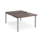 Large modular bench desk with a dark wood-effect top, integrated cable access cut-out, and silver metal legs, shown on a white background.
