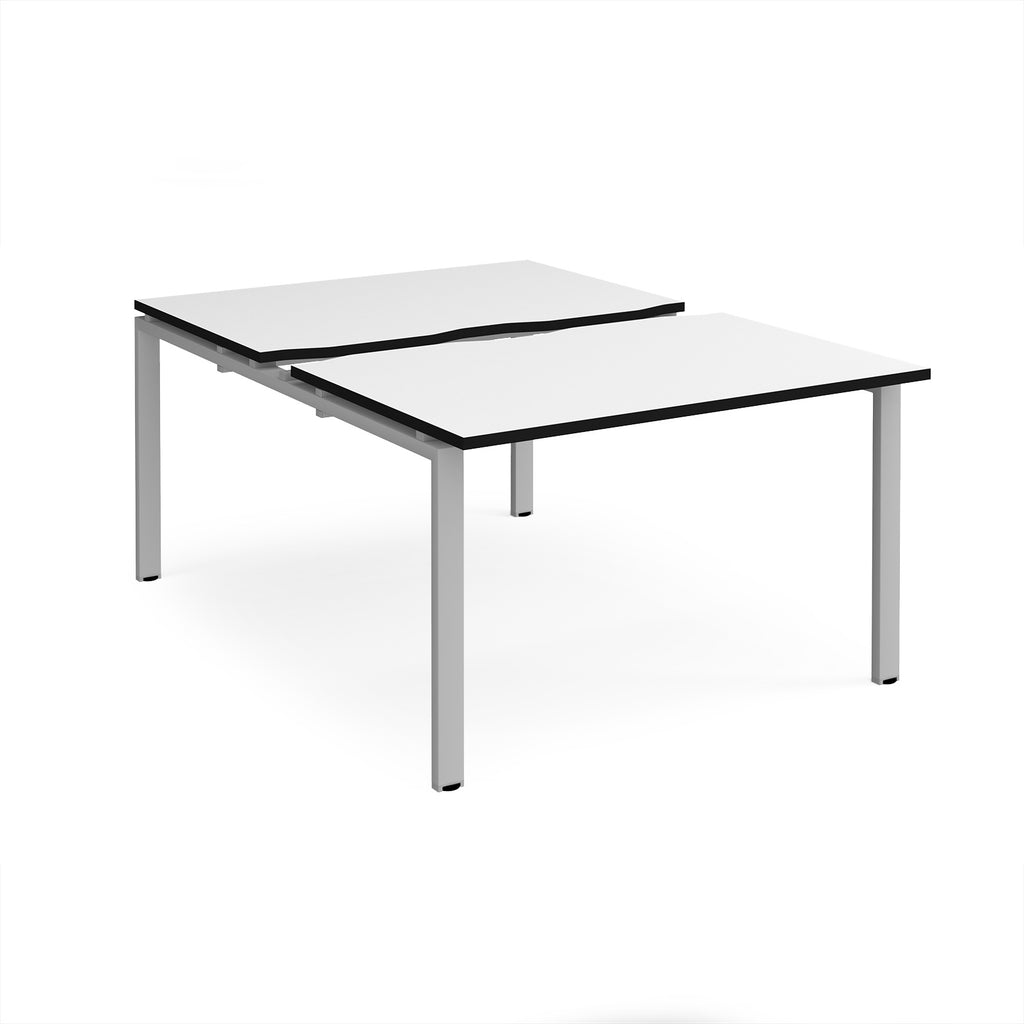 Large modular bench desk with a white worktop, contrasting black edge detail, integrated cable access cut-outs, and silver metal legs, shown on a white background.