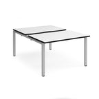 Large modular bench desk with a white worktop, contrasting black edge detail, integrated cable access cut-outs, and silver metal legs, shown on a white background.