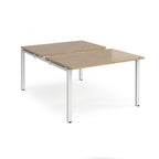 Large modular bench desk with a wood-effect top, integrated cable access cut-out, and white metal legs, shown on a white background.