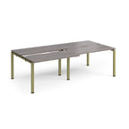 Large modular bench desk with a grey wood-effect top, integrated cable access slots, and green metal legs, shown on a white background.