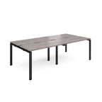 Large modular bench desk with a grey wood-effect top, integrated cable access cut-outs, and black metal legs, shown on a white background.