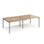 Large modular bench desk with a wood-effect top, integrated cable access cut-outs, and silver metal legs, shown on a white background.
