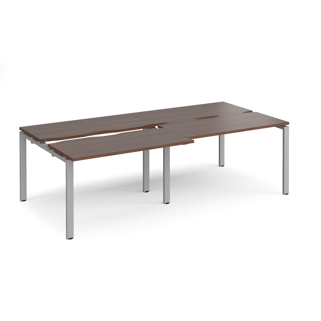 Large modular bench desk with a dark wood-effect top, integrated cable access cut-outs, and silver metal legs, shown on a white background.
