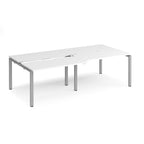Large modular bench desk with a white worktop, integrated cable access cut-outs, and silver metal legs, shown on a white background.