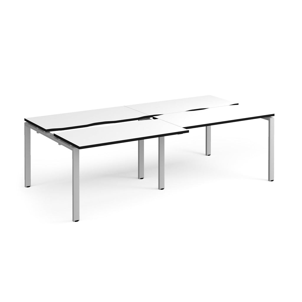Large modular bench desk with a white worktop, contrasting black edge detail, integrated cable access cut-outs, and silver metal legs, shown on a white background.