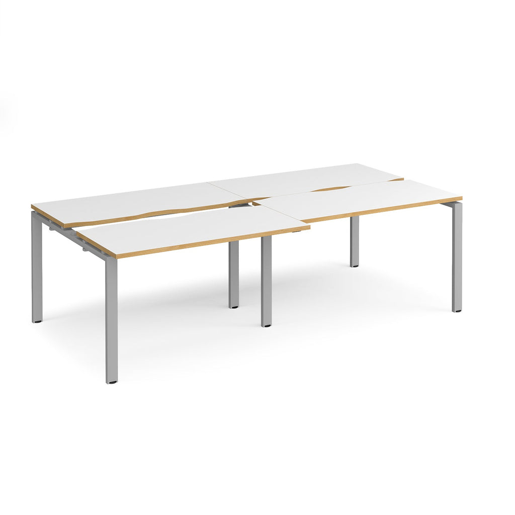 Large modular bench desk with white panels and wood-effect edging, integrated cable access cut-outs, and silver metal legs, shown on a white background.