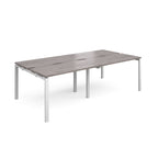 Large modular bench desk with a grey wood-effect top, integrated cable access slots, and white metal legs, shown on a white background.