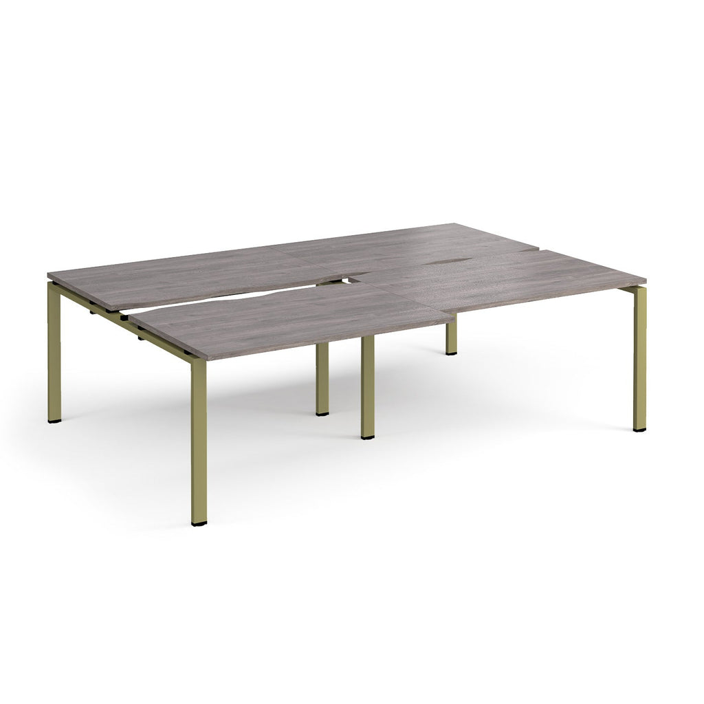 Large modular bench desk with a grey wood-effect top, integrated cable access slots, and green metal legs, shown on a white background.