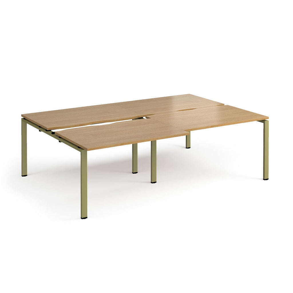 Large modular bench desk with a light wood-effect top, integrated cable access cut-outs, and green metal legs, shown on a white background.