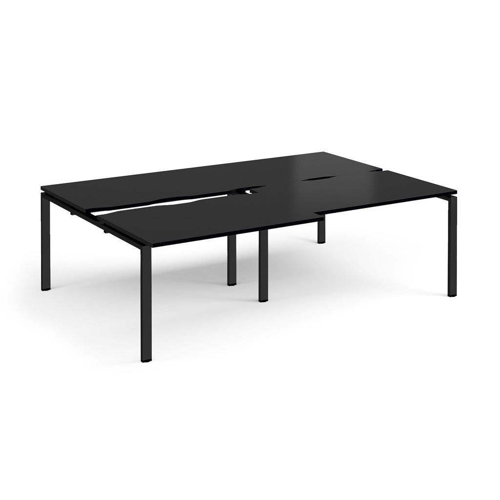 Large modular bench desk with a black worktop, integrated cable access cut-outs, and matching black metal legs, shown on a white background.