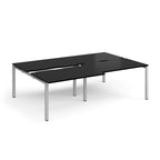 Large modular bench desk with a black worktop, integrated cable access cut-outs, and silver metal legs, shown on a white background.