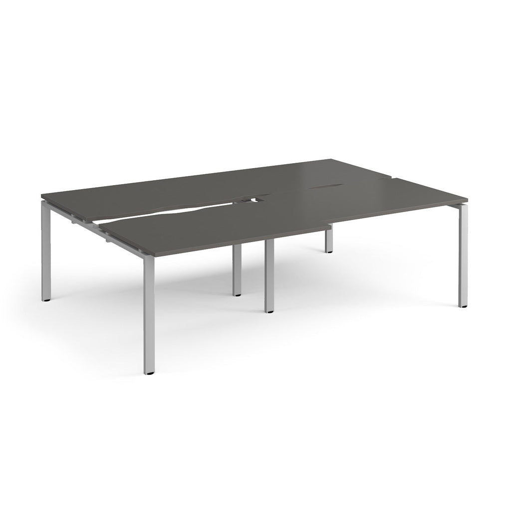 Large modular bench desk with a grey worktop, integrated cable access cut-outs, and silver metal legs, shown on a white background.