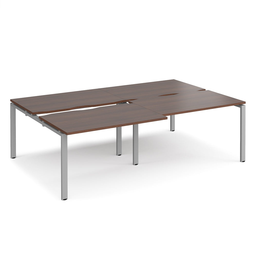 Large modular bench desk with a dark wood-effect top, integrated cable access cut-outs, and silver metal legs, shown on a white background.