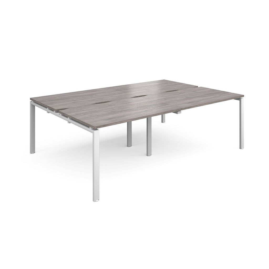 Large modular bench desk with a grey wood-effect top, integrated cable access slots, and white metal legs, shown on a white background.