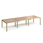 Large modular bench desk with a light wood-effect top, integrated cable access cut-outs, and green metal legs, shown on a white background.