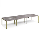 Large modular bench desk with a grey wood-effect top, integrated cable access slots, and green metal legs, shown on a white background.