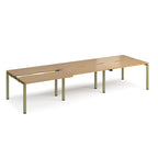 Large modular bench desk with a light oak wood-effect top, integrated cable access cut-outs, and green metal legs, shown on a white background.