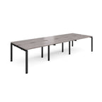 Large modular bench desk with a grey wood-effect top, integrated cable access slots, and black metal legs, shown on a white background.