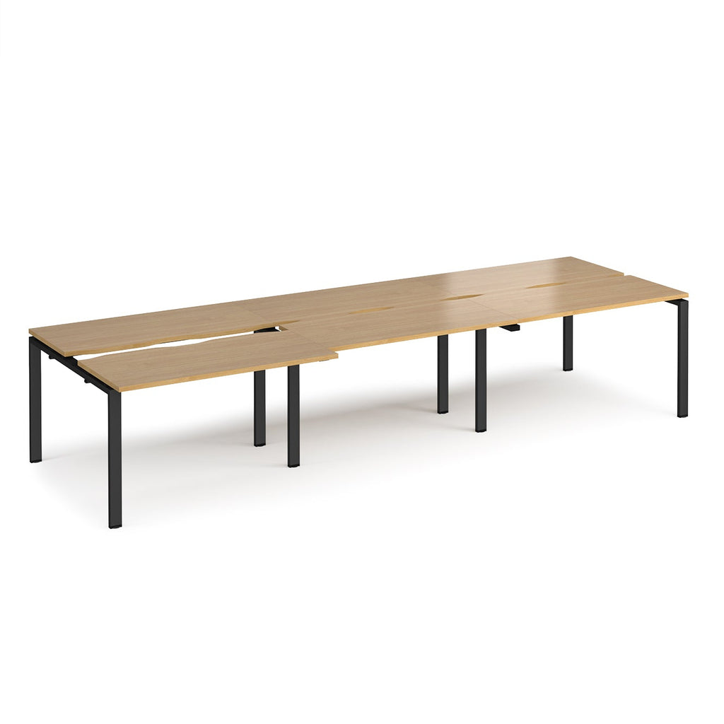 Large modular bench desk with wood-effect panels, integrated cable cut-outs, and black metal legs, shown on a white background.