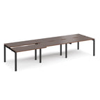 Large modular bench desk with dark wood-effect panels, integrated cable cut-outs, and black metal legs, shown on a white background.

