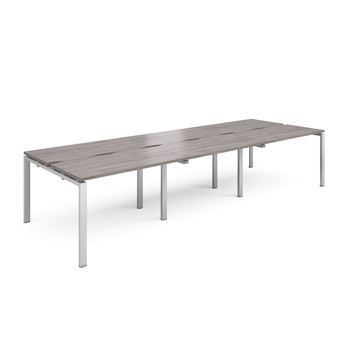 Large modular bench desk with a grey wood-effect top, integrated cable access slots, and silver metal legs, shown on a white background.