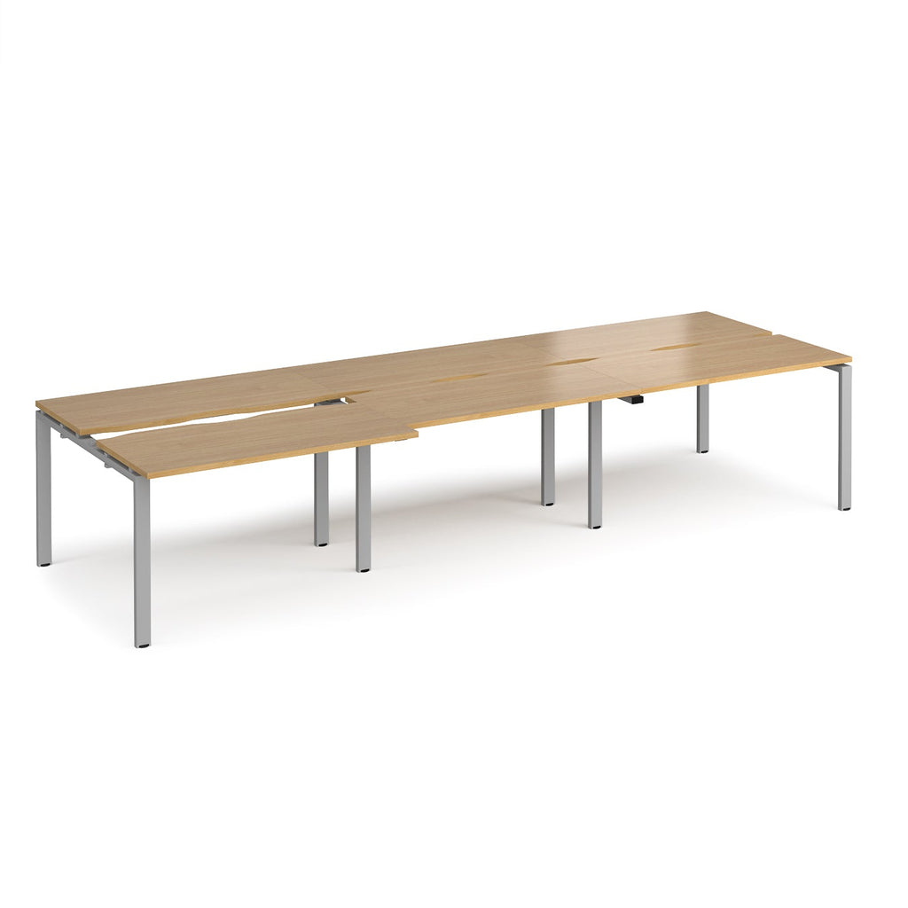 Large modular bench desk with a light wood-effect finish, integrated cable access cut-outs, and sturdy grey metal legs, shown on a white background.