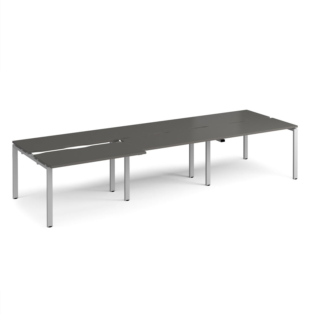 Large modular bench desk with a grey worktop, integrated cable access cut-outs, and silver metal legs, shown on a white background.