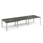 Large modular bench desk with a grey worktop, integrated cable access cut-outs, and silver metal legs, shown on a white background.