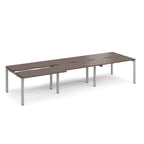 Large modular bench desk with dark wood-effect panels, integrated cable cut-outs, and silver metal legs, shown on a white background.