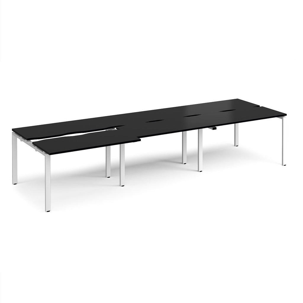 Large modular bench desk with a black worktop, integrated cable access cut-outs, and white metal legs, shown on a white background.
