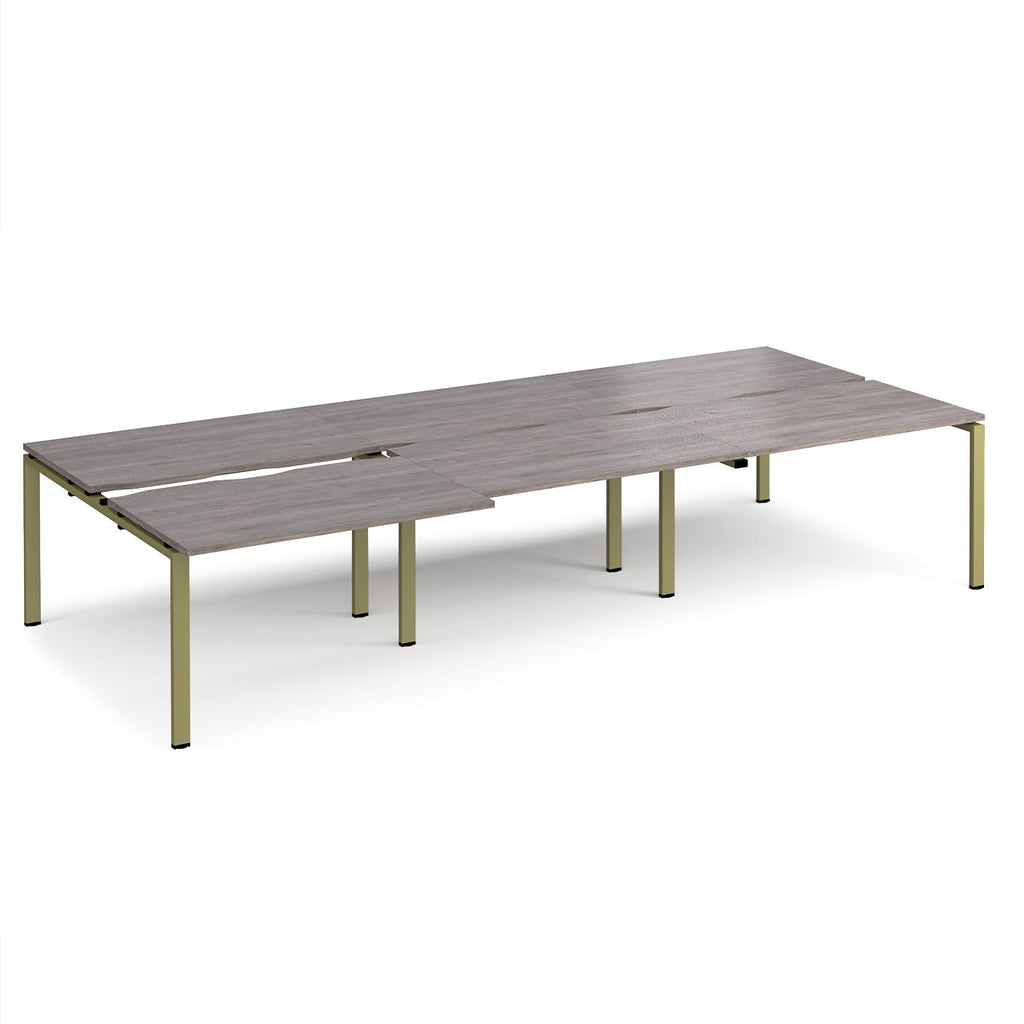 Large modular bench desk with a grey wood-effect top, integrated cable access slots, and green metal legs, shown on a white background.