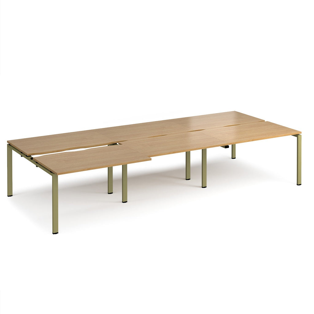 Large modular bench desk with a light oak wood-effect top, integrated cable access cut-outs, and green metal legs, shown on a white background.