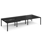 Large modular bench desk with a black worktop, integrated cable access cut-outs, and black metal legs, shown on a white background.