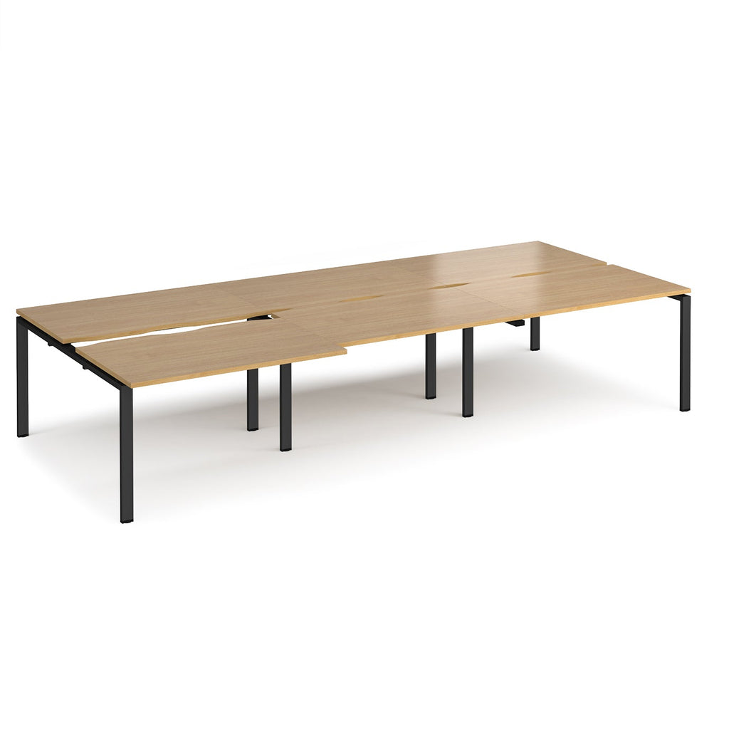 Large modular bench desk with a light oak wood-effect top, integrated cable access cut-outs, and black metal legs, shown on a white background.