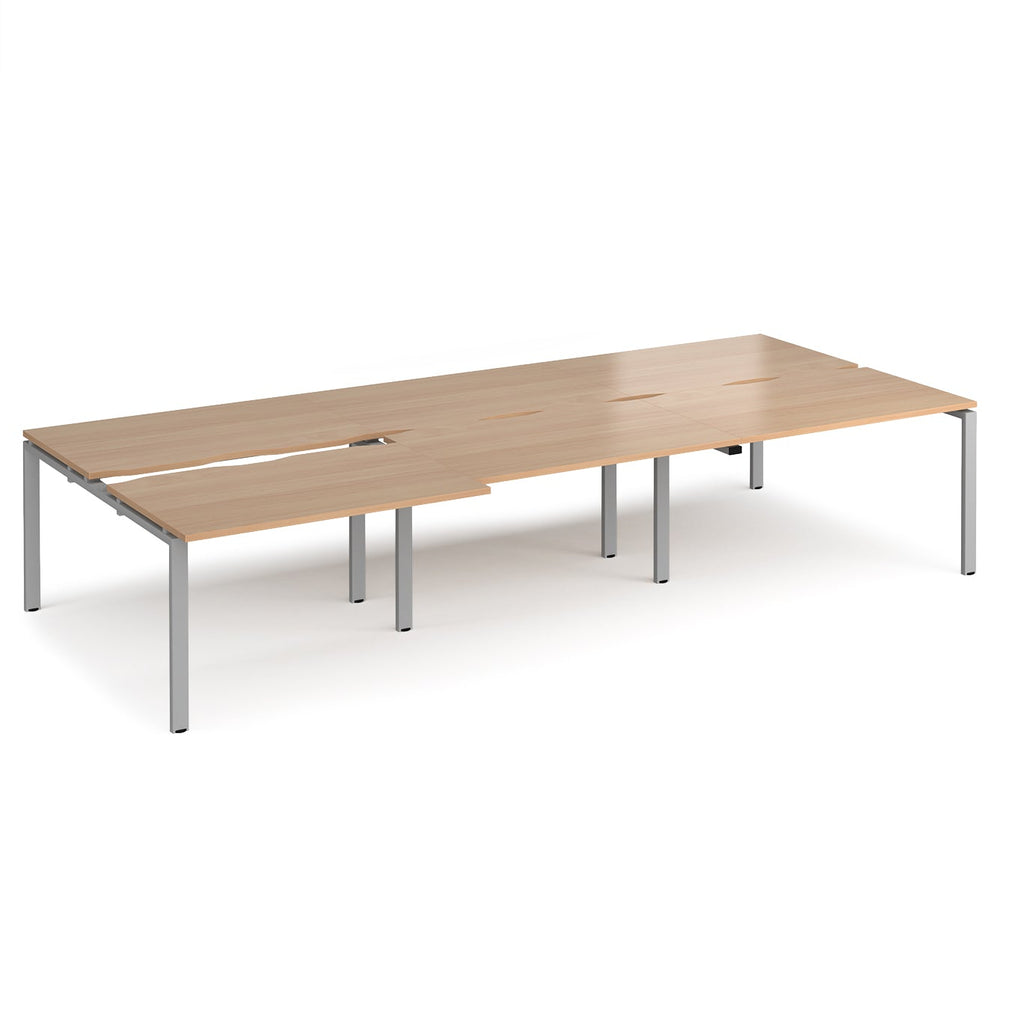 Large modular bench desk with a light wood-effect top, integrated cable access cut-outs, and silver metal legs, shown on a white background.