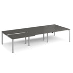 Large modular bench desk with a dark grey worktop, integrated cable access cut-outs, and silver metal legs, shown on a white background.