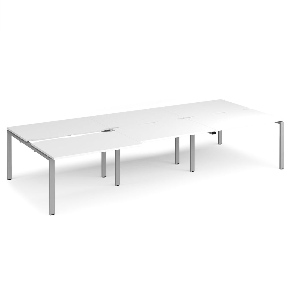 Large modular bench desk with a white worktop, integrated cable access cut-outs, and silver metal legs, shown on a white background.