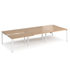 Large modular bench desk with a light wood-effect top, integrated cable access cut-outs, and white metal legs, shown on a white background.