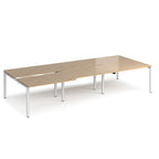 Large modular bench desk with a light oak wood-effect top, integrated cable access cut-outs, and white metal legs, shown on a white background.
