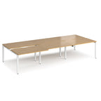 Large modular bench desk with a light oak wood-effect top, integrated cable access cut-outs, and white metal legs, shown on a white background.