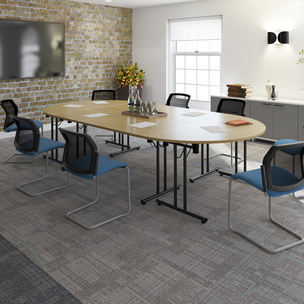 Modern meeting room with oval wooden table, blue conference chairs, wall-mounted screen, and brick feature wall.