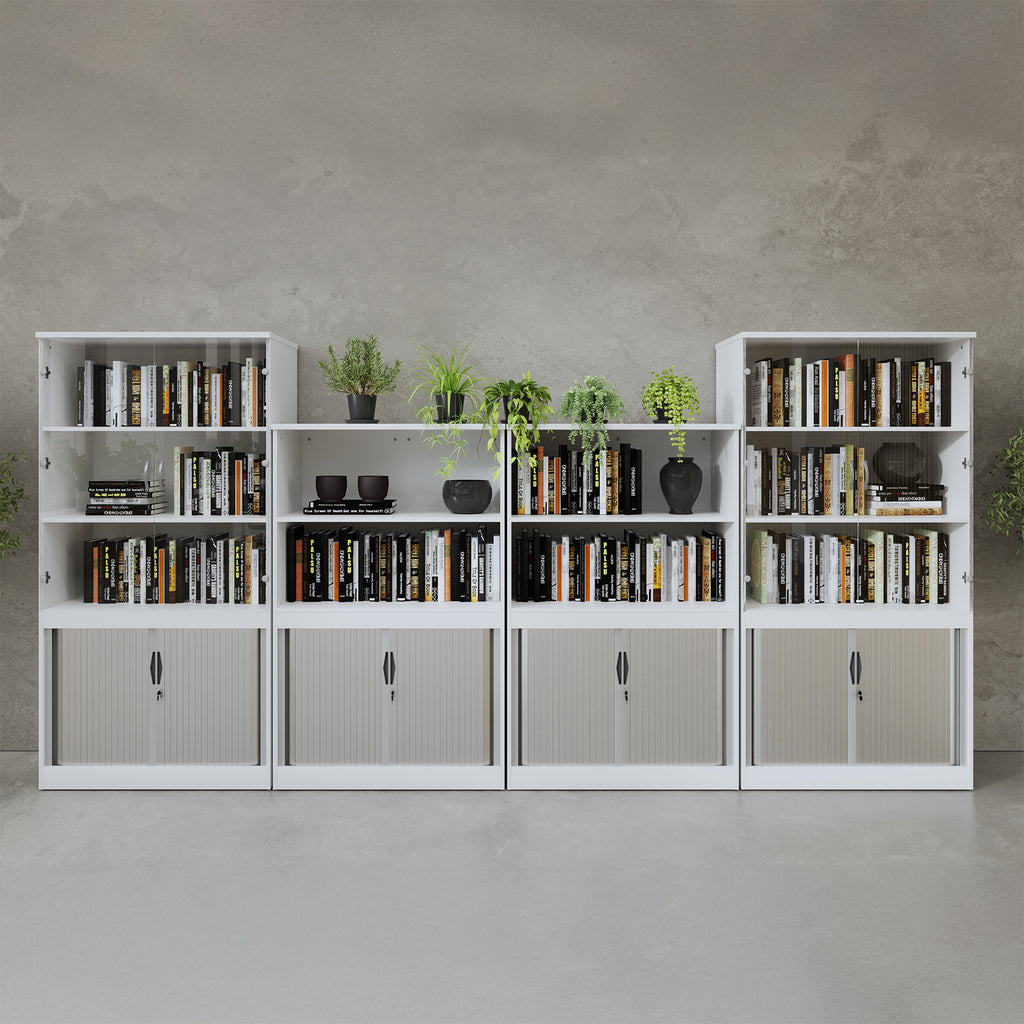 Row of white office bookcases with open shelving and lockable tambour doors, filled with books and decorative plants, arranged against a concrete-style wall.