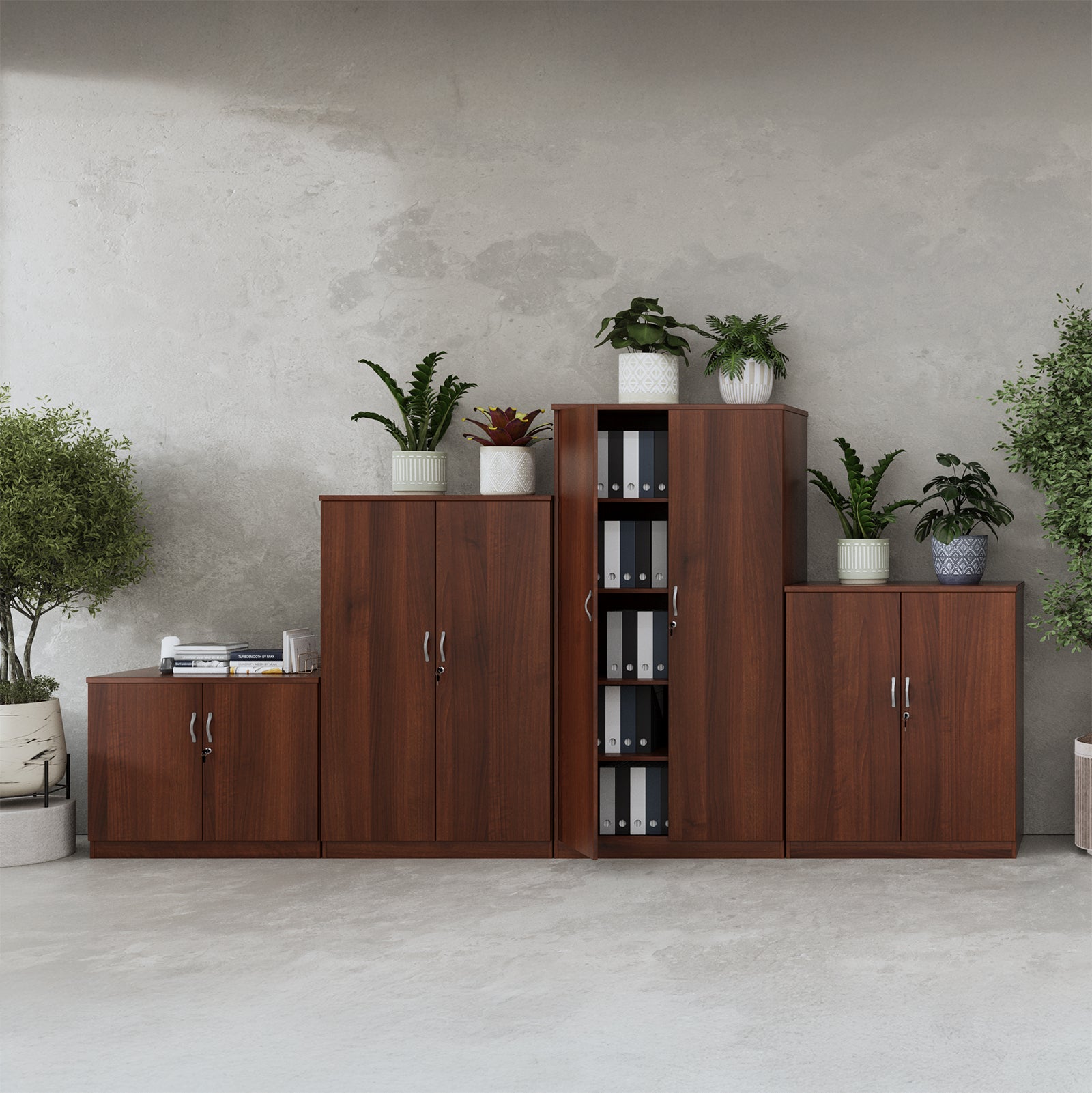 A set of modern wooden office storage cabinets in a warm brown finish, arranged against a textured grey concrete wall with potted plants and books as styling props.