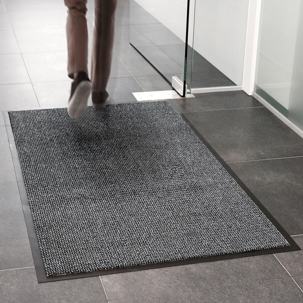 Person stepping onto a gray doormat in a tiled room.